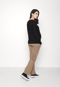 Top preto com texturas, de mangas compridas, combinado com calças bege e sapatilhas pretas. O top tem um decote arredondado e as calças possuem bolsos laterais.