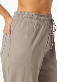 Ljust bruna joggers i mjukt tyg, med resårmidja, dragsko, sidofickor och subtila vertikala sömmar.