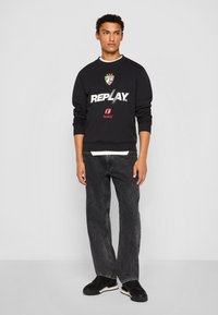 Black sweatshirt with white "REPLAY" logo, red accent, and emblem. Paired with dark gray jeans and black shoes. Simple, casual design.