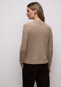 Pull beige côtelé avec un col rond, des manches longues et un ourlet légèrement court, associé à un pantalon foncé.
