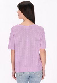Lila, cable-knit pulóver rövid ujjakkal, laza szabással, bordás aljjal és texturált mintával. Világoskék farmernadrággal viselve.