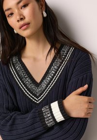 Pulover de marină cu dungi, cu decolteu în formă de V, având accente contrastante în alb și negru pe guler și pe manșete, dintr-un material tricotat texturat.