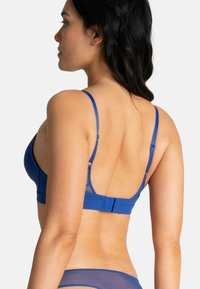 Soutien-gorge sans fil bleu avec bretelles réglables, texture lisse et fermeture au dos par crochet et œillet. Le design présente un style épuré et minimaliste.