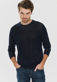 Granatowy sweter dzianinowy z długimi rękawami, okrągłym dekoltem i ściągaczami na mankietach. Materiał wydaje się lekki i nieco przezroczysty.