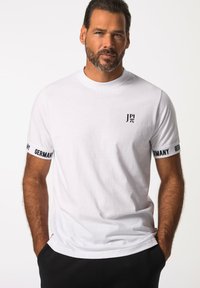 Valkoinen puuvillapaita, jossa on pyöreä kaula-aukko, ja joissa on mustat tekstit "JP π" ja "Saksa" hihoissa. Rentomallinen, jonka pinta on sileä.