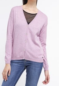 Light pink cardigan made of soft material, featuring a deep V-neck, long sleeves, and five front buttons. Worn over a black mesh top.
