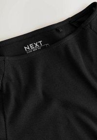 Black ribbed slash neck top featuring a smooth texture, fitted design, and a label visible on the neckline.