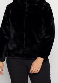 Zwarte jas van nepbont met een hoge kraag, volledige ritssluiting en lange mouwen. Het materiaal heeft een zachte, fluweelachtige textuur en een gladde afwerking.