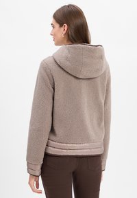 Brown faux-shearling jacket with a hood, ribbed cuffs, and a smooth, shiny bottom hem. The fabric is textured and warm-looking.