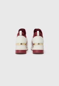 Sneakers bianchi e bordeaux con una tomaia in pelle liscia, caratterizzati da un accento dorato sul tallone e una linguetta per facilitare l'indossamento.