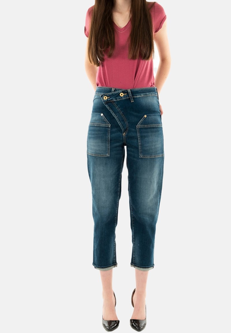 Jeans cropped en denim bleu foncé avec poches avant, une fermeture éclair angulaire unique et des accents de boutons dorés. Texture lisse et délavée.