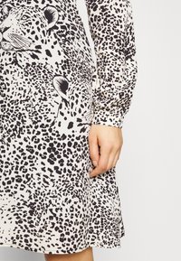 Sukienka w panterkę wykonana z miękkiego, lekkiego materiału, z długimi rękawami i rozszerzanym dołem, w odcieniach kremu i czerni.
