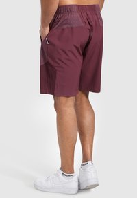 Bordeauxrote Sportshorts mit einem strukturierten Bund und Seitentaschen. Kombiniert mit weißen Sneakers. Glattes Material.