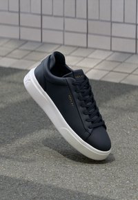 Navyblaue synthetische Leder-Sneaker mit einer weißen Gummisohle, runder Zehenform und Schnürdesign; verfügt über 'REPLAY'-Branding in Gold.