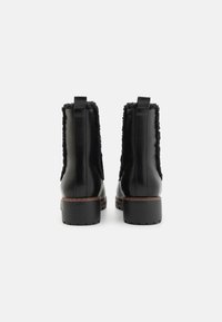 Bottines en cuir noir avec des détails en shearling, bout rond, languette de tirage et semelle en caoutchouc texturée. Accents cousus en marron.