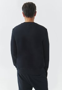 Sudadera negra con cuello redondo, puños y dobladillo acanalados; textura suave, con un diseño sutil y un corte relajado.