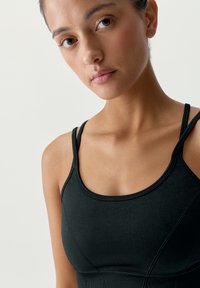 Svart atletisk crop-top med tunna remmar, med en mjuk textur och konturerade sömmar, designad för komfort under fysiska aktiviteter.