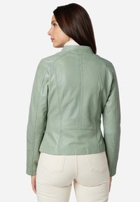 Mintgrön läderjacka med en figursydd design, som har subtila sömnadsdetaljer och en ståkrage. Slät textur och skräddarsydd form.
