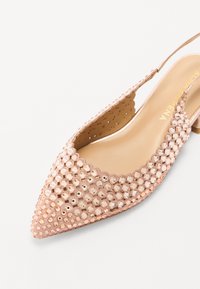 Zapato de punta afilada en color rosa con tira trasera, que presenta una parte superior decorada con strass y un interior liso de color claro con bordes ondulados.