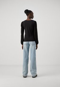 Svart topp med teksturerte puffeerm, parret med lyseblå høy midje-jeans. Sette har en avslappet passform og minimal detaljer.