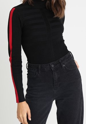 Zwarte geribbelde coltrui met horizontale strepen en rode zijaccenten, gecombineerd met hoge taille zwarte jeans.