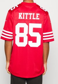 Camiseta de fútbol roja con detalles en blanco. La parte de atrás muestra "KITTLE" y el número "85" en letras blancas en negrita. Mangas cortas con franjas blancas.