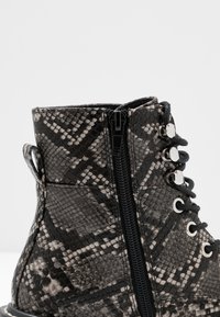 Bottine à cheville imprimé serpent noir et gris avec surface texturée, fermeture éclair, œillets en métal et languette à l'arrière pour un enfilage facile.