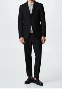 Zwart op maat gemaakte broekpak met een blazer met één knoop, een grijze ronde hals trui en zwarte schoenen; gladde stof, gestructureerde vorm, minimalistisch ontwerp.