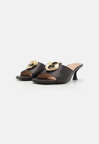 Black open-toe mules featuring curved front design, gold heart-shaped embellishments, and a small, block heel. Textured material with a smooth finish.