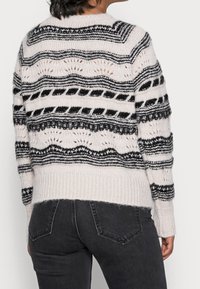 Personne portant un pull en tricot blanc avec des rayures horizontales noires et des motifs, associé à un jean gris foncé, vue de dos.