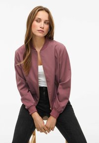 Burgundijas bomberis ar priekšējo rāvējslēdzēju, ribotiem piedurkņu galiem un gludu auduma tekstūru, kombinēts ar baltu augšdaļu un melnām biksēm.