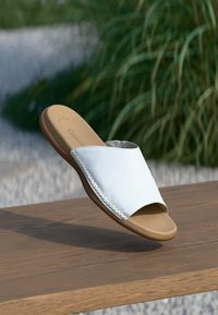 Bílé kožené skládací sandály s otevřenou špičkou, texturovaným povrchem a pleteným akcentem podél okraje, s hnědou podrážkou a polstrovanou stélkou.