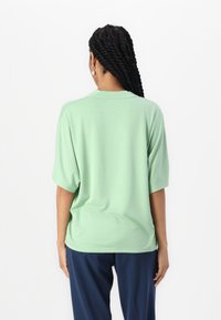 T-shirt a maniche corte, verde menta, con una vestibilità comoda, collo tondo e tessuto morbido. Indossato con pantaloni blu navy, caratterizzati da una texture liscia.