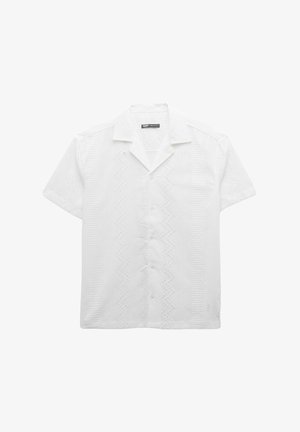 Chemise blanche à manches courtes avec des motifs en zigzag texturés, un devant à boutons et un col de style camp.