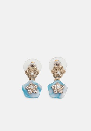 Pendientes de botón con diseño floral en tono dorado, adornados con piedras de imitación claras y perlas, colgando de piezas de resina en forma de flor azul.