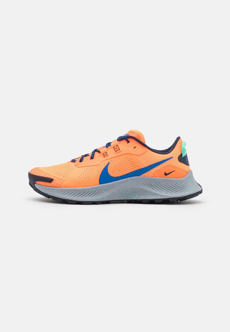 Chaussure de course Nike orange vif avec un swoosh bleu, des lacets noirs et bleus, une semelle grise avec des taches vertes, et un détail noir au talon.
