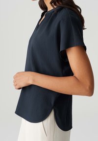 T-shirt à manches courtes bleu marine avec un motif texturé, doté d'un col en V et d'un ourlet arrondi. Fabriqué en tissu léger, il tombe de manière fluide.