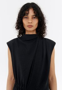 Black sleeveless dress with a draped neckline and slight gathering. The fabric features subtle dotted texture. Lightweight, fluid design.