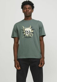 T-shirt en coton vert avec un graphique sur le devant représentant un crâne, agrémenté de divers éléments de design, complété par des manches courtes et une coupe décontractée.