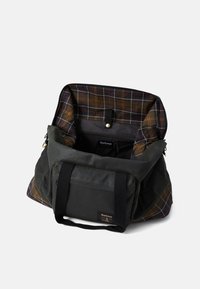 Dark green Barbour tote bag with black handles, open to reveal multicolored plaid interior lining and inner zippered pocket.
