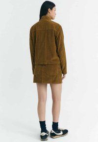 Brown corduroy jacket with a matching skirt, featuring vertical ribbing. Model wears black sneakers and knee-length socks.