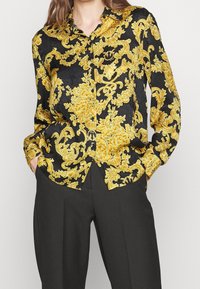 Koszula z guzikami, z czarnym tłem i w detaliczne złote wzory kwiatowe oraz spirale. Długie rękawy i klasyczny krój kołnierzyka.