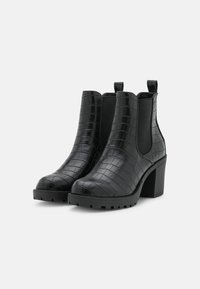 Bottines noires à texture embossée façon croco, talon épais, panneaux élastiques latéraux et languettes de tirage. Semelle en caoutchouc pour adhérence et durabilité.