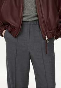 Burgundy leather bomber jacket paired with gray elastic-waist trousers featuring a subtle texture and side pockets. Silver zipper detail visible.
