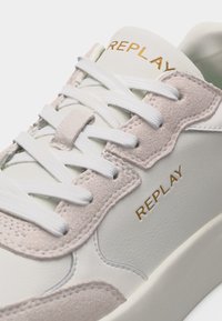 Άσπρο αθλητικό παπούτσι με μπεζ σουέντ επενδύσεις, λευκά κορδόνια και το λογότυπο "REPLAY" σε χρυσό στη γλώσσα και την πλαϊνή πλευρά.