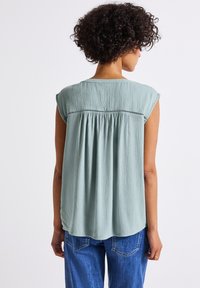 Lichtgroene top met korte mouwen van textuurstof en een geplooide achterkant, gecombineerd met blauwe jeans. Eenvoudig en ontspannen ontwerp.