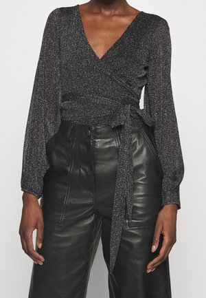 Top avvolgente nero e luccicante con maniche lunghe e trasparenti e scollatura a V. Legato in vita, abbinato a pantaloni in pelle a vita alta.