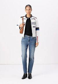 Casaco de couro branco com apliques, detalhes azuis e vermelhos, camisa preta, jeans de ganga azul e botas pretas de tornozelo. Bolsa de ombro castanha.