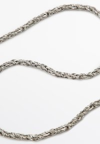 Metal halskæde med en flettet design, der har en sølvfarvet finish. Kjeden har en struktureret overflade og glatte kanter, der fremhæver detaljeret vævning.
