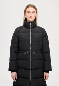 Cappotto puffer nero con colletto alto, cuciture diagonali, chiusura con zip e due toggles frontali. Presenta un design trapuntato e maniche lunghe.
